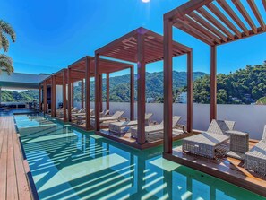 Un espace piscine aménagé sur le toit, avec des chaises longues et des pergolas en bois, offrant une vue sur de luxuriantes collines verdoyantes.