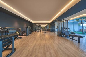 A modern gym with wooden flooring, various exercise equipment, and a view of the outdoors through large windows. - NEW Luxury Modern Condo in SOHO PV! Best Rooftop! (Puerto Vallarta)