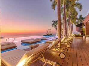 Un resort con piscina infinita, sillas de descanso y palmeras.