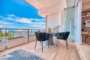 A balcony with a dining table and chairs, a view of the sea, and a modern interior design.