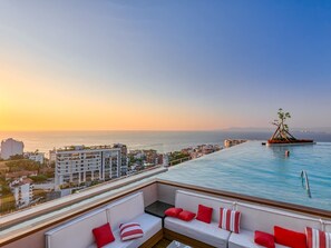 Une piscine à débordement située sur le toit, offrant une vue sur la ville et l’océan au coucher du soleil.