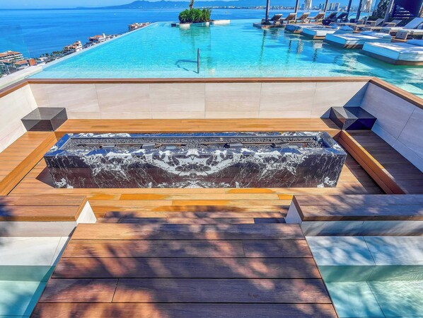 Zona de piscina con vistas al mar, terraza de madera y fuente de agua.