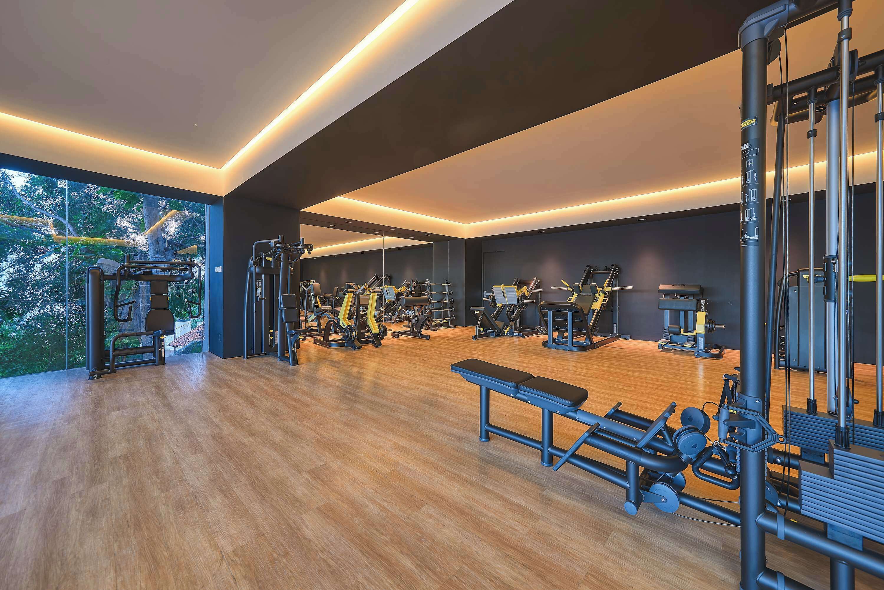 Una palestra moderna con diverse attrezzature per esercizi, ampie finestre e pavimento in legno.