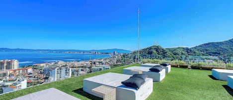 A rooftop lounge area with outdoor seating and a view of the city and coastline.