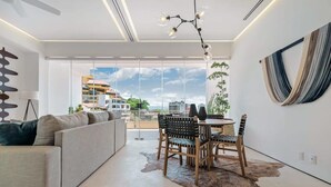 Un salon moderne comprenant un canapé, une table à manger, des chaises et offrant une vue sur le paysage urbain grâce à de grandes fenêtres.