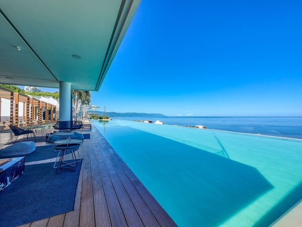 Ein Infinity-Pool mit freiem Blick auf den Ozean, eine Holzterrasse, Liegestühle und Sonnenschirme.