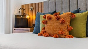 Un lit avec un oreiller orange à texture, un oreiller vert et un oreiller bleu.