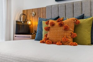Ein Bett mit einem orangefarbenen, strukturierten Kissen, einem grünen Kissen und einem blauen Kissen.
