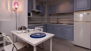 A modern kitchen with white cabinets, a white refrigerator, and a dining area with a white table and chairs. - San Marino 28 - Studio (Los Cristianos)