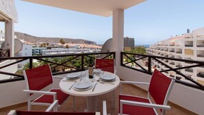 A balcony with a table set for dining, overlooking a coastal area with buildings and hills. - San Marino 28 - Studio (Los Cristianos)