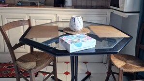 A small kitchen with a microwave, coffee maker, and a shelf with various items. There is a glass table with a box and two wicker chairs. - Un Appartementspacieux Calme Limite Vincennes (Fontenay-sous-Bois)