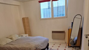 A bedroom with a bed, a standing heater, a window with red curtains, and a mirror. - Un Appartementspacieux Calme Limite Vincennes (Fontenay-sous-Bois)