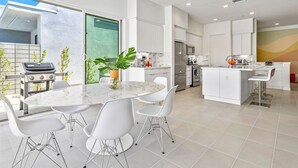 A modern kitchen with white cabinetry, a central island with seating, and a dining area with a marble table and white chairs.