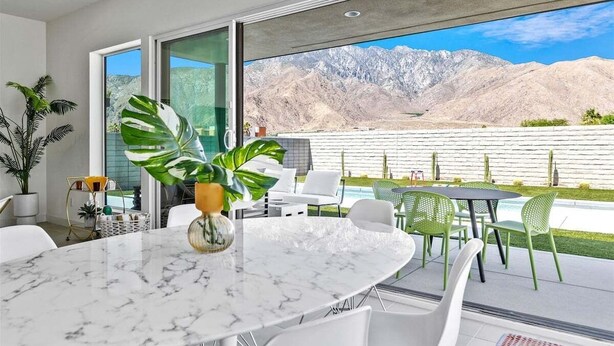 A modern outdoor dining area with a marble table, white chairs, and a large potted plant.
