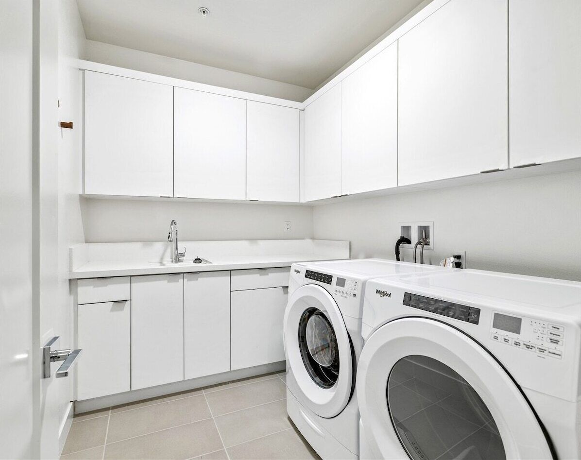 A modern laundry room with a front-loading washer and dryer, white cabinetry, and a tiled floor.