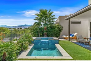 A swimming pool with a view of mountains, surrounded by a well-maintained lawn and a patio with lounge chairs.