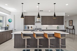 A modern kitchen with a central island, bar stools, pendant lighting, and a clock on the wall. - Skyline Views at Miralon - Palm Springs Perfection: Relax, Play & Recharge in a Gated Community (Palm Springs)