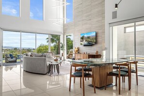 A modern living room with a glass dining table, sofas, and a large TV mounted on the wall.