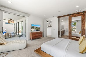 A modern bedroom with a large bed, a sofa, a wooden dresser, and a sliding glass door leading to a balcony. - Skyline Views at Miralon - Palm Springs Perfection: Relax, Play & Recharge in a Gated Community (Palm Springs)