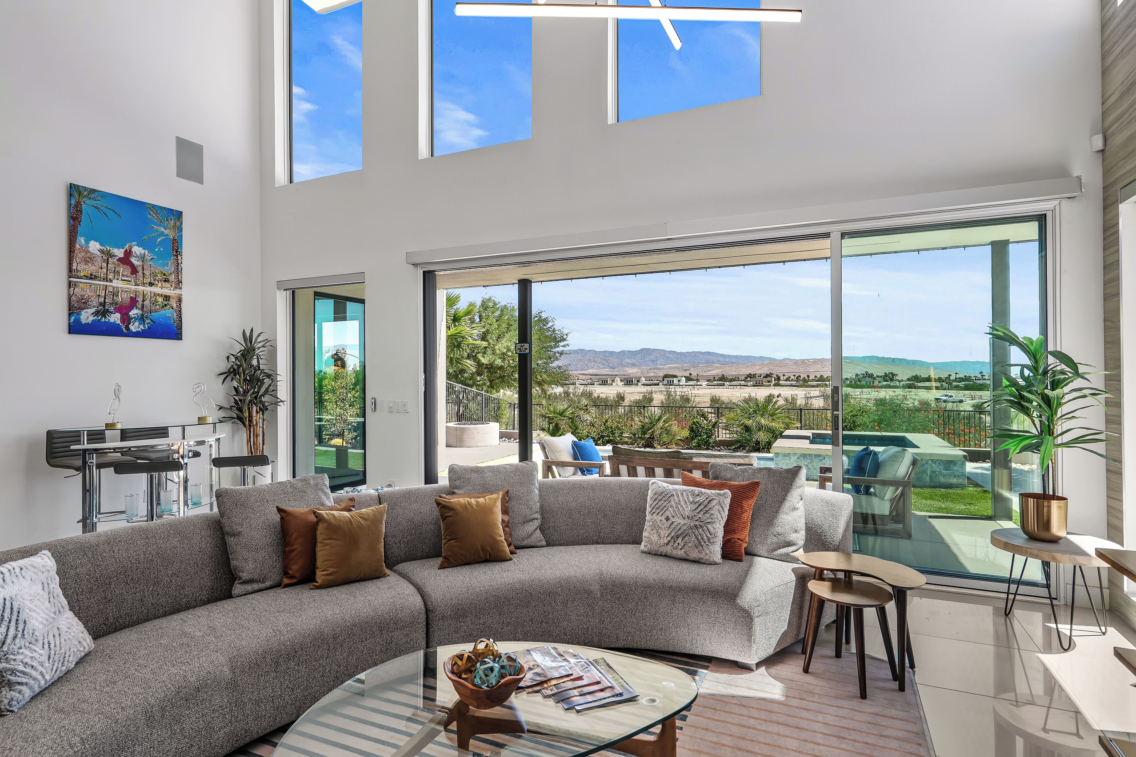 Una sala de estar moderna con un sofá seccional, una mesa de centro de vidrio y ventanas amplias que ofrecen vistas a un jardín.