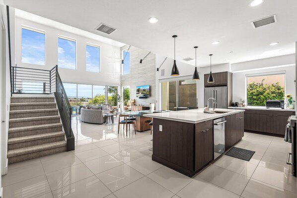 A modern kitchen with a central island, dark cabinetry, and a dining area with a view.