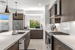 A modern kitchen with a central island, stainless steel appliances, and a view of greenery outside.