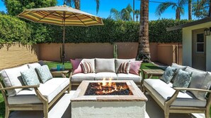 An outdoor patio with a fire pit, two sofas, and an umbrella.
