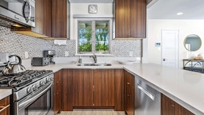 A modern kitchen with wooden cabinets, a stainless steel stove, and a window with a view of trees.