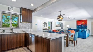 A modern kitchen with a large island, wooden cabinets, and a dining area with a blue sofa and patterned cushions.