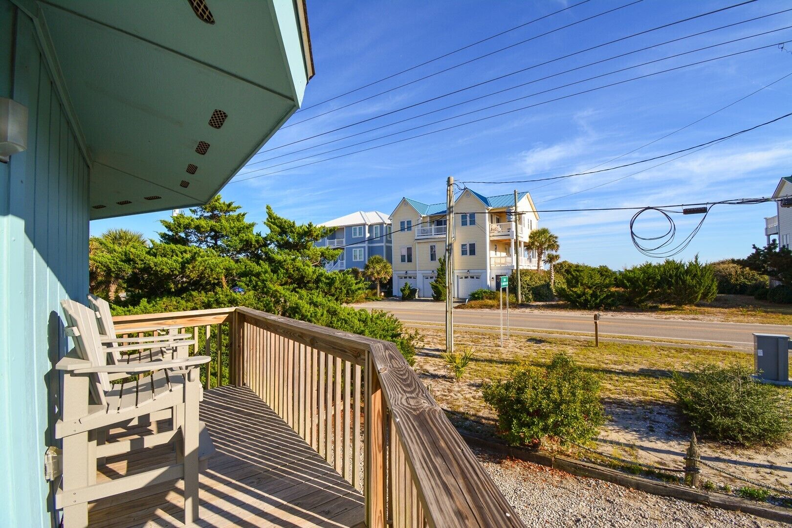 A wooden deck with a view of a beachfront property, including a house with a balcony and a clear sky.