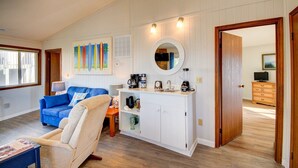 Un salon avec un canapé bleu, un fauteuil beige, un meuble blanc avec un miroir et une machine à café.