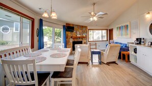 Un coin repas avec une table et des chaises blanches, une cheminée en pierre et un ventilateur de plafond.