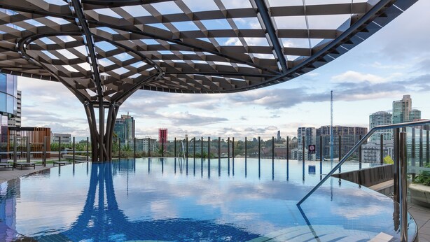 An indoor infinity pool with a modern metal canopy structure, surrounded by city buildings. - Mega Style Apartments Melbourne Square (Southbank)