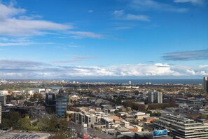 A cityscape with a mix of modern and older buildings, a clear sky, and a distant view of the sea. - Mega Style Apartments Melbourne Square (Southbank)