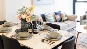 A dining table set with plates, bowls, cutlery, wine glasses, and a bottle of wine. - Mega Style Apartments Melbourne Square (Southbank)