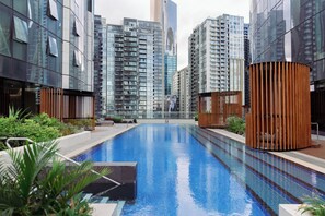 A modern building with a swimming pool surrounded by greenery and tall residential buildings in the background. - Mega Style Apartments Melbourne Square (Southbank)