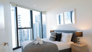 A modern bedroom with a large window, a neatly made bed, and a bedside table with a lamp. - Mega Style Apartments Melbourne Square (Southbank)