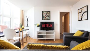 A modern living room with a flat-screen TV, a dining area with a table and chairs, and a sofa with yellow cushions. - Smart Apartments - King's House (Southampton)