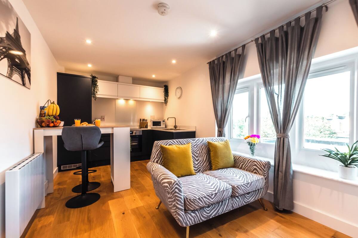 A modern apartment with a kitchen, dining area, and a sofa with cushions.