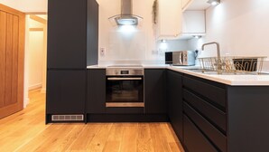 A modern kitchen with dark cabinetry, a stainless steel range hood, a built-in oven, a microwave, and a sink with a gold faucet. - Smart Apartments - King's House (Southampton)