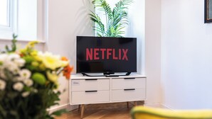 A living room with a white TV stand, a flat-screen TV displaying 'NETFLIX', and a potted plant. - Smart Apartments - King's House (Southampton)