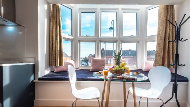 A dining area with a glass table, two white chairs, a fruit bowl, and a view through large windows. - Smart Apartments - King's House (Southampton)