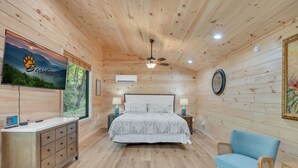 Een slaapkamer met houten lambrisering, een bed, bedlampen, een televisie, een dressoir en een stoel.