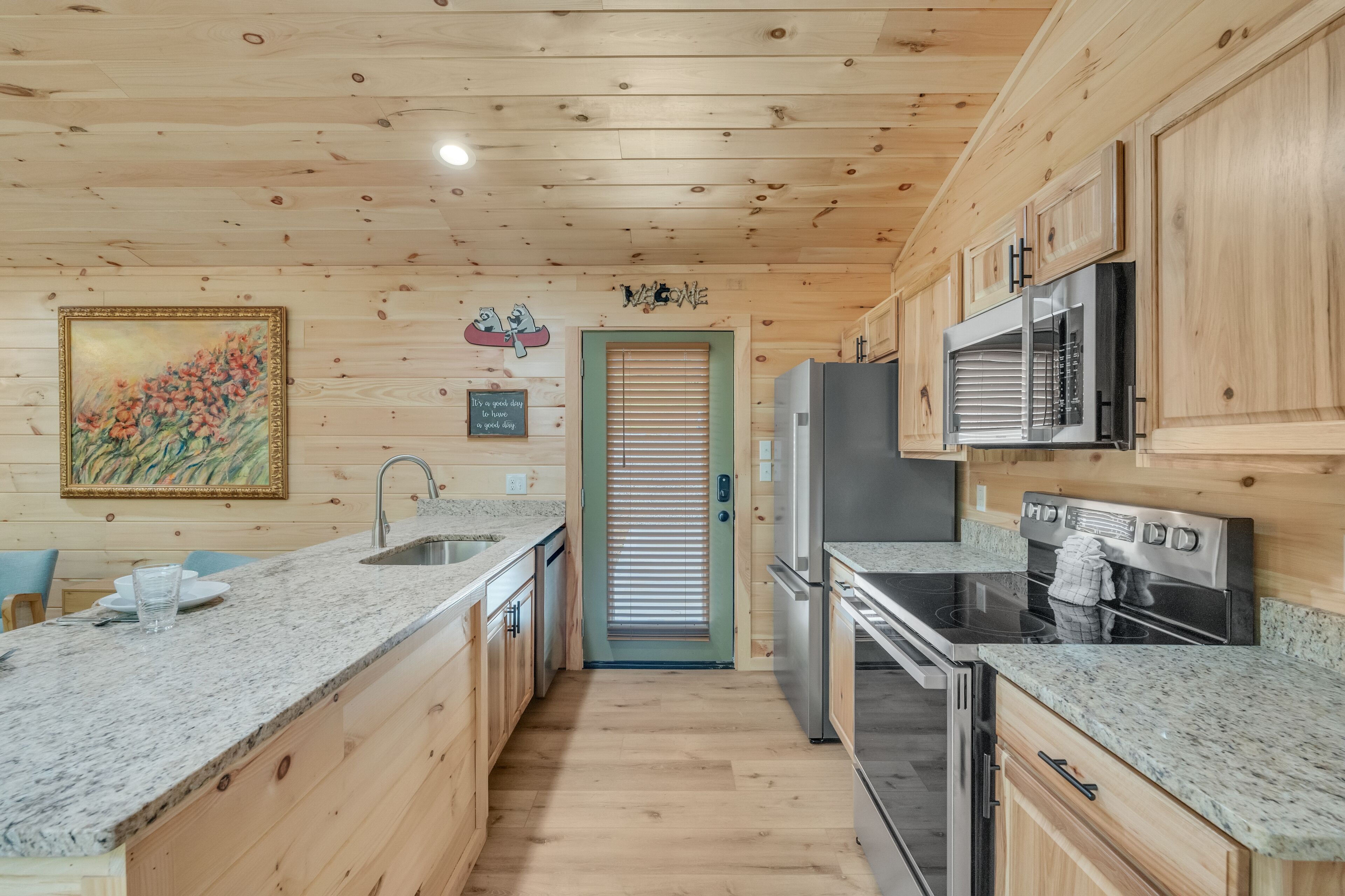 A kitchen with wooden walls, granite countertops, stainless steel appliances, and a framed painting.