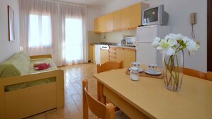A compact living space with a kitchenette, a dining area, and a sofa. - Holiday apartment mit Klimaanlage und Balkon (Bibione)