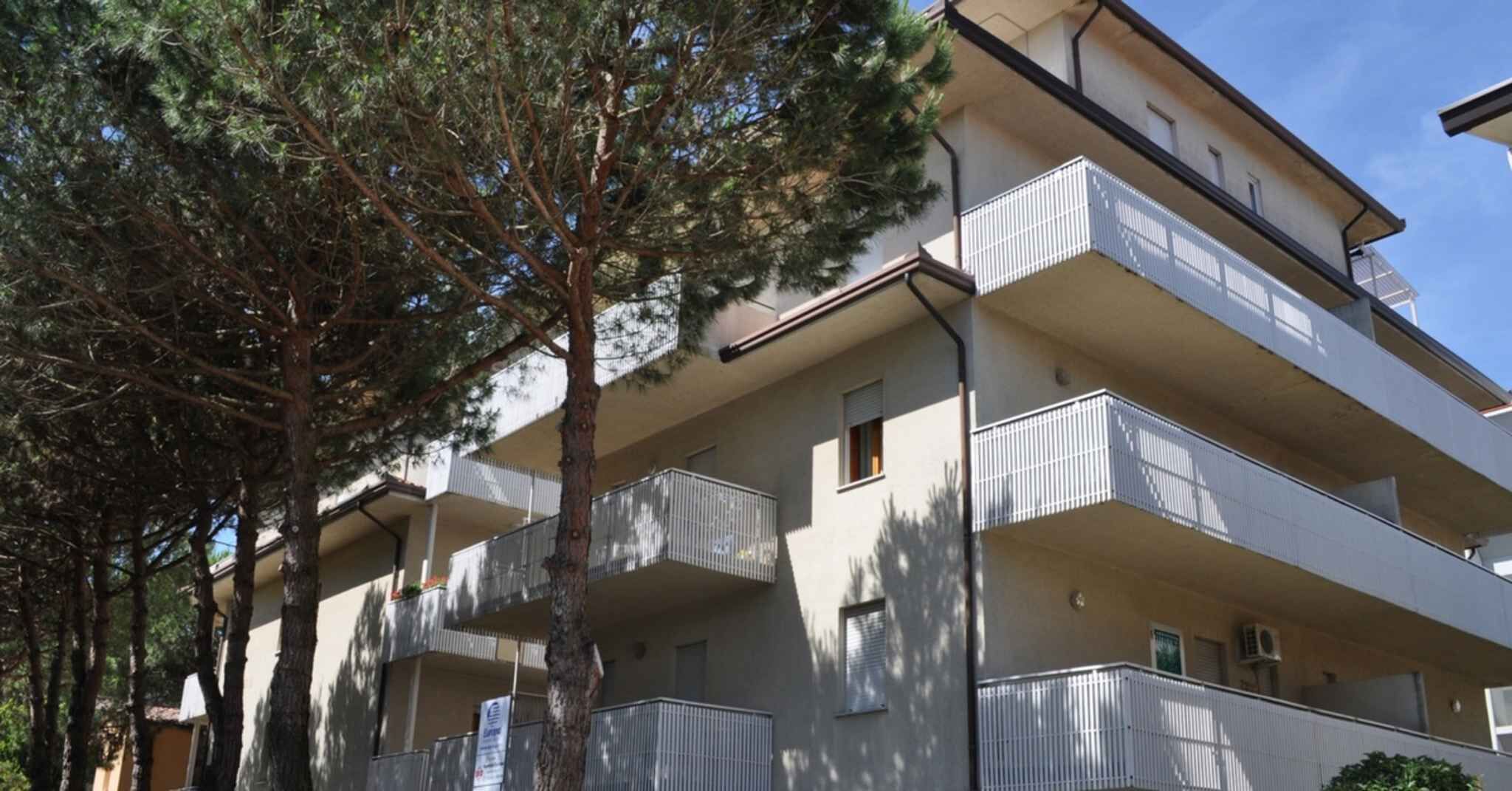 Un immeuble résidentiel à plusieurs étages, doté de balcons et entouré d’arbres.