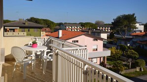 A balcony with a table and chairs, overlooking a residential area with various buildings. - Holiday apartment mit Klimaanlage und Balkon (Bibione)