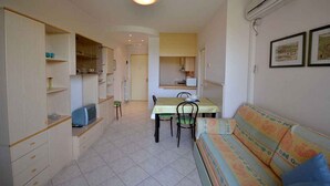 A compact living space with a dining area, kitchenette, and a sofa. - Holiday apartment with air conditioning and balcony (Bibione)