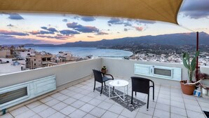 Ein Balkon mit Blick auf das Meer und die Berge, ausgestattet mit einem Tisch, Stühlen, einem Blumentopf und Sonnenschirm.