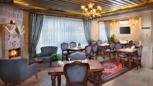 A dining area with a fireplace, multiple dining tables, chairs, and a chandelier. - Cappadocia Pyramid Stone House (Nevsehir)